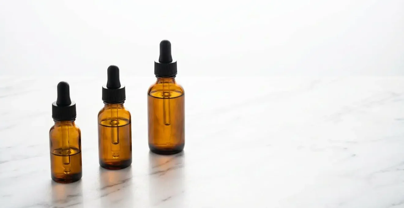 Trois flacons d'huile CBD de concentrations différentes alignés sur une surface minimaliste avec ombre douce